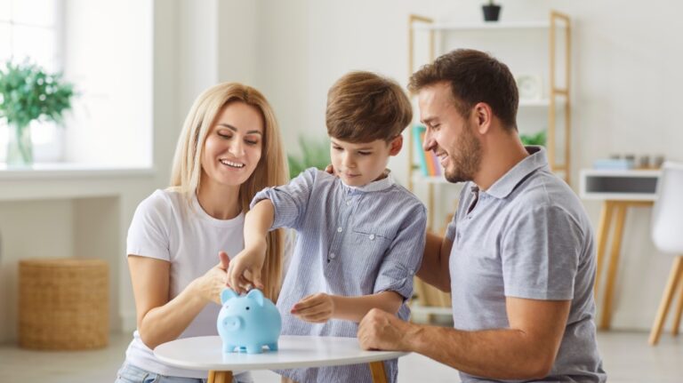 Parents and child together put a coin into a piggy bank, teaching savings and financial habits. This family moment of saving money occurs in home, showcasing unity and planning together.