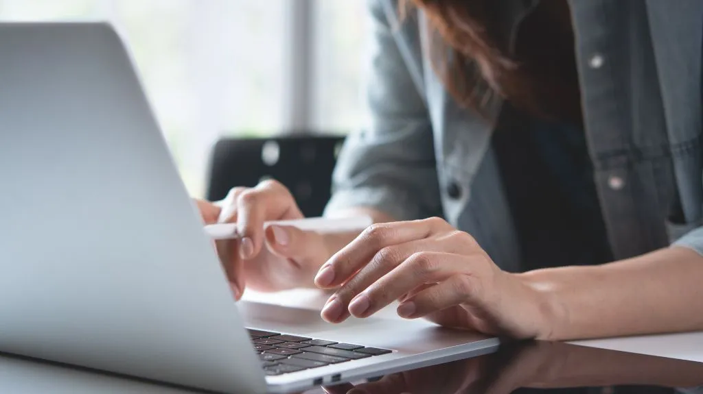Close-up of a person typing on a silver laptop keyboard in a well-lit indoor setting.