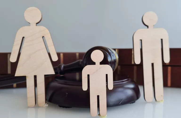 Wooden figurines of a woman, man, and child in front of a judge's gavel and law books.