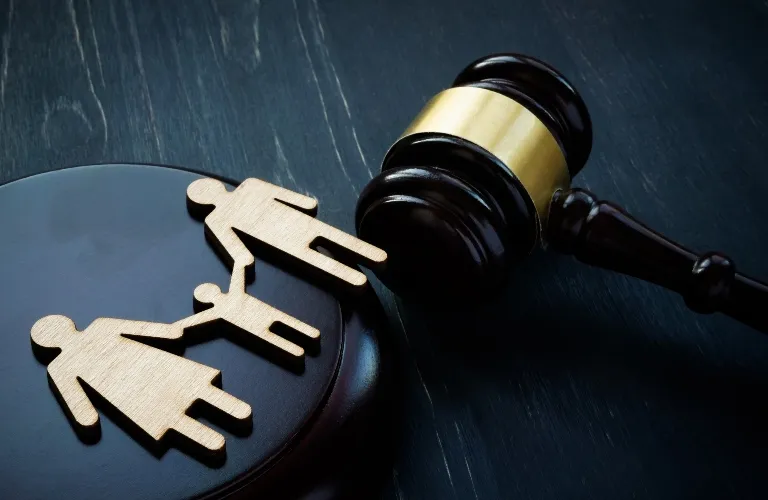 Wooden cutouts of a family holding hands next to a dark wooden judge's gavel on a black surface.